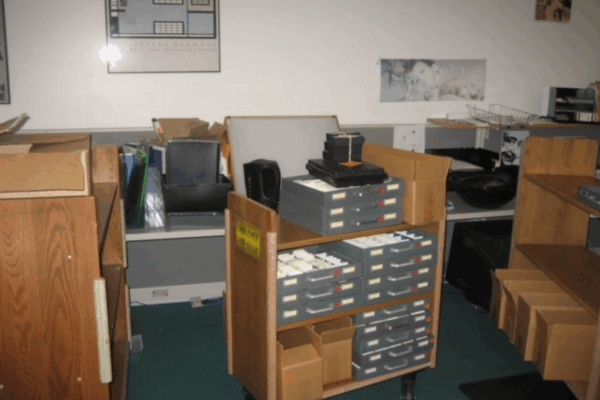 Library or archive workspace with carts and shelves holding boxes and drawers of photographic slides and equipment.