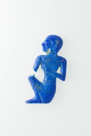 A cobalt blue hieroglyph of a person sitting down and looking to the left. The inlay piece is chipped. 