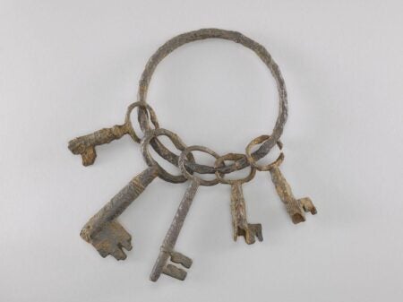 A set of six rusted iron keys on a circular keyring, likely from the late 18th to mid-19th century, displayed on a neutral background. The keys vary in size and shape, with visible wear and corrosion, suggesting long-term use and historical significance.
