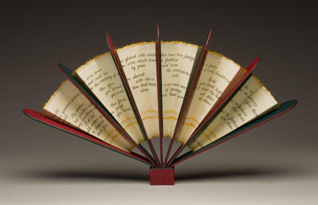 An artist’s book opened in a fan shape, with pages inscribed in elegant script and painted edges, radiating outward from a red spine.