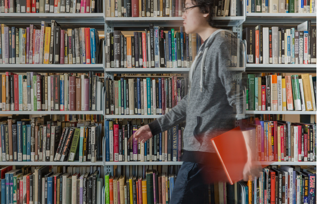 Man holding a book walking past a bookcase in a library