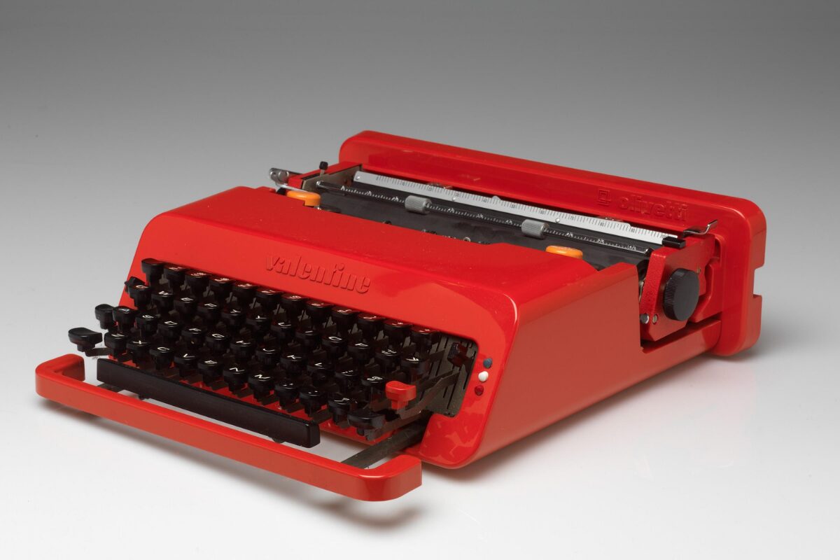 Bright red Olivetti “Valentine” typewriter with black keys and a sleek, modern plastic casing, shown angled on a white surface.