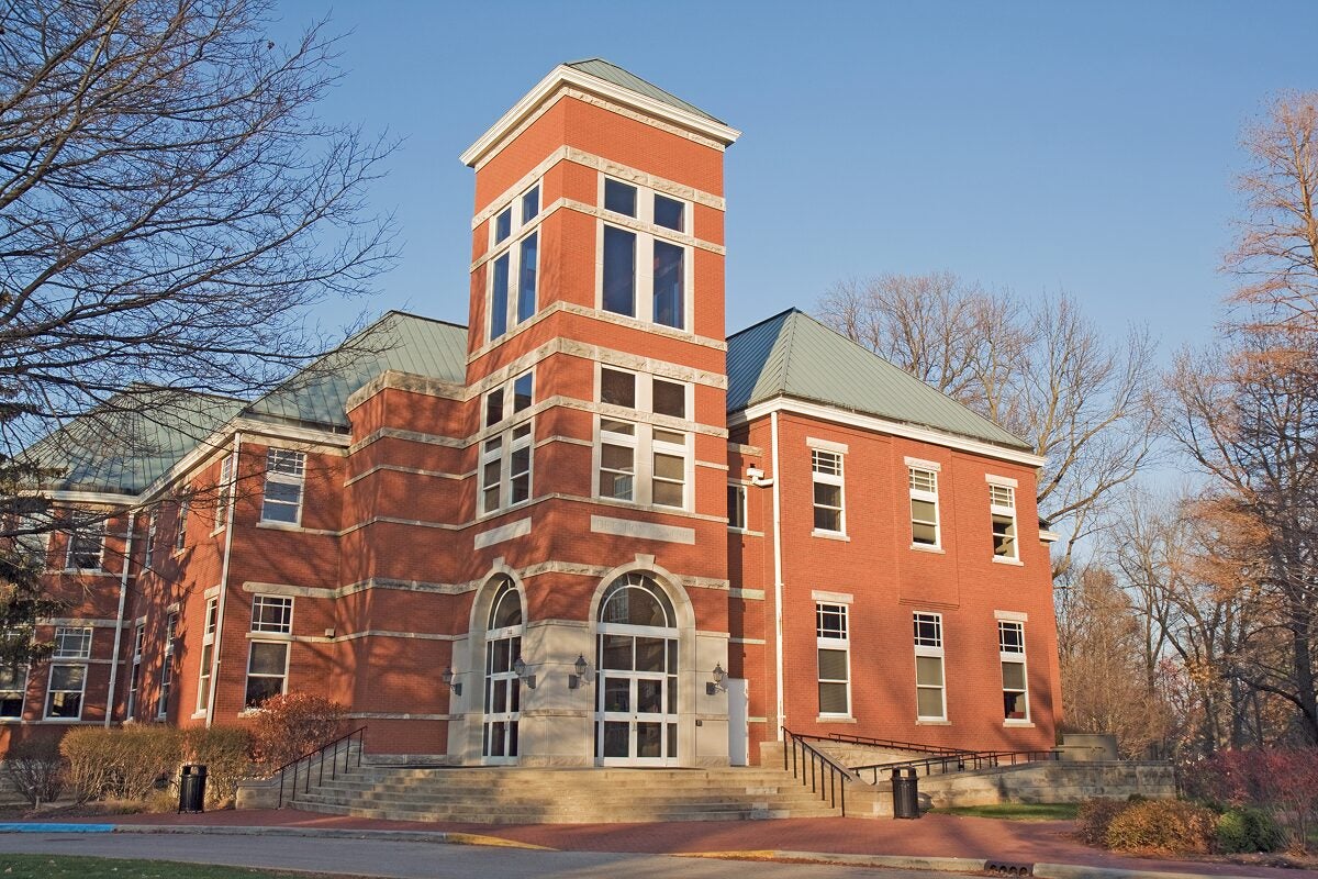 Exterior of a brick academic building with large windows and a green roof on a sunny day.