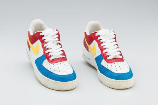 A pair of Nike sneakers in white with bright red, blue, and yellow suede panels, shown from the front.