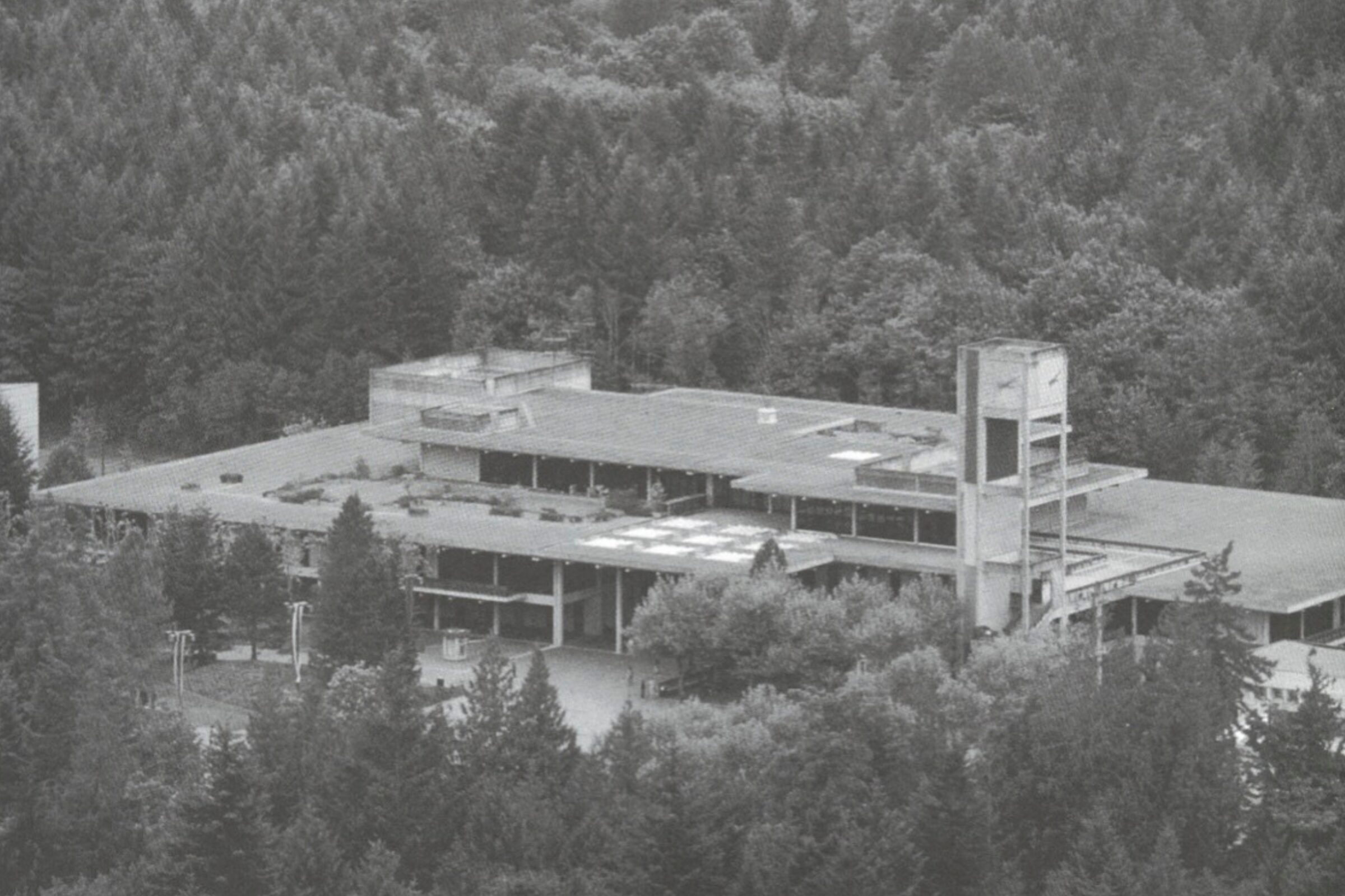 Black-and-white aerial photograph of The Evergreen State College campus surrounded by dense forest and hills.